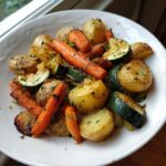 A white bowl filled with perfectly roasted Garlic Herb Roasted Veggies, including golden potatoes, bright carrots, and zucchini slices.