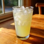 A tall glass filled with homemade lemonade and plenty of ice cubes, glistening in the sunlight.