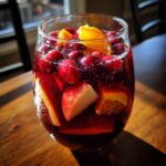 Close-up of a glass filled with bubbling red Christmas sangria, loaded with cranberries, orange slices, and apple chunks.