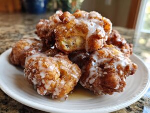 A stack of golden brown, freshly fried apple fritter pieces drizzled generously with white glaze.