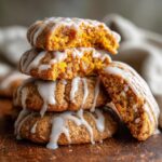 A stack of four soft, spiced persimmon cookies drizzled with white glaze, one cookie is broken to show the moist interior.
