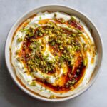 Overhead view of a creamy ricotta dip swirled with honey and topped generously with chopped green pistachios.