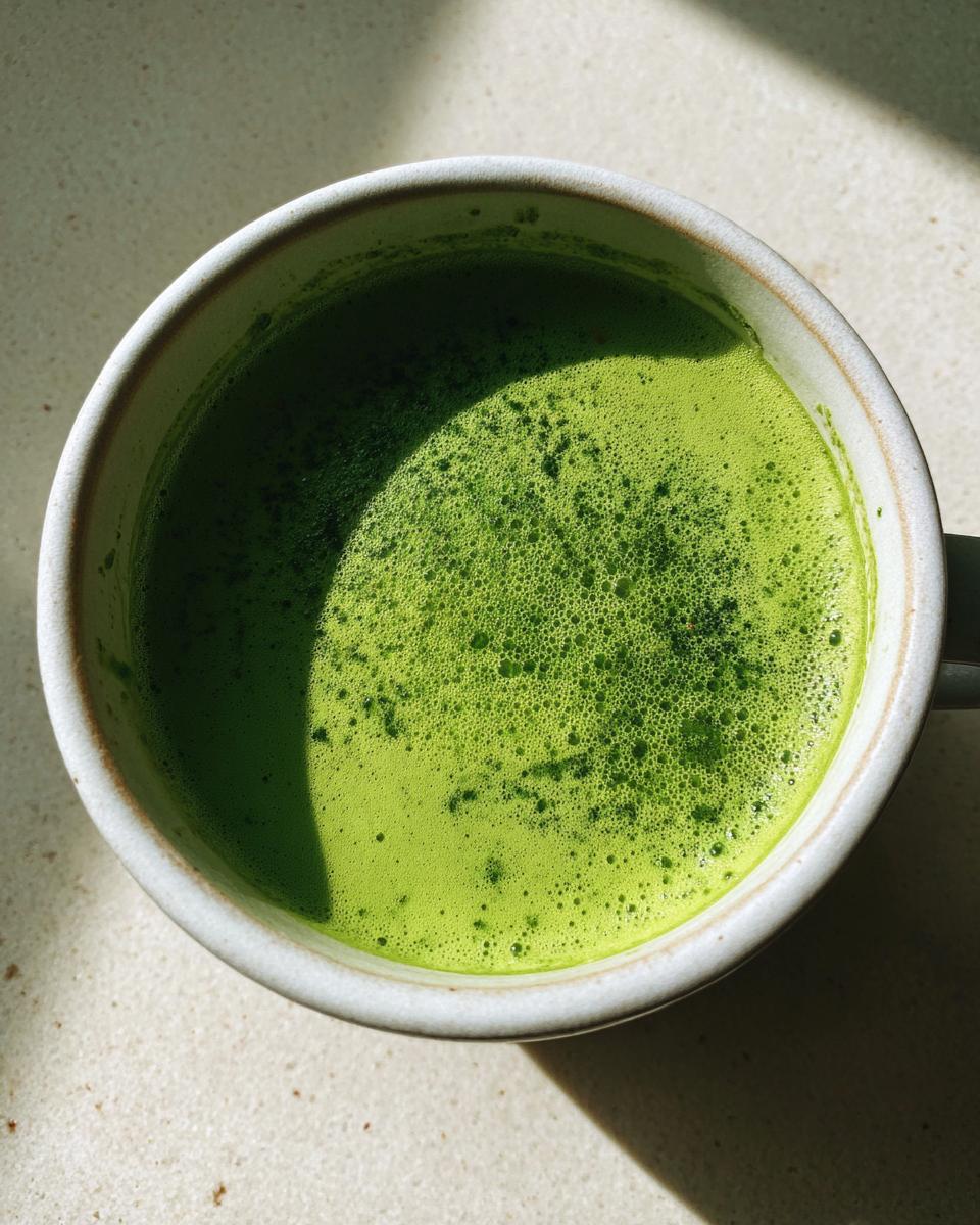 Overhead view of a bright green, frothy beverage, possibly matcha, in a light-colored mug, contrasting with the article's asparagus soup keyword.