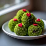 A stack of bright green Grinch Oreo balls coated in green crumbs and topped with small red hearts.