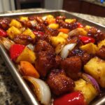 Close-up of sticky, glazed hawaiian chicken sheet pan with pineapple chunks, red peppers, and onions.