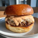 Close-up of a juicy burger dripping with creamy, orange burger sauce on a brioche bun.