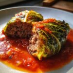 Close-up of two cabbage rolls cut in half, revealing the savory meat filling, served in rich tomato sauce.