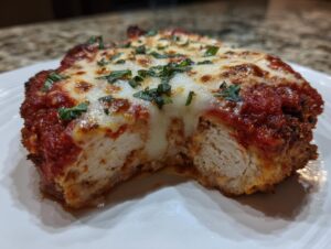 Close-up of keto chicken parmesan showing the thick, white chicken breast interior, topped with melted mozzarella, marinara sauce, and basil.
