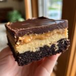 A person holding a thick, three-layer buckeye brownies square with a rich chocolate top.