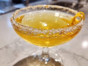 Close-up of a bright yellow lemon drop martini in a coupe glass with a thick, sparkling sugar rim and lemon twist garnish.