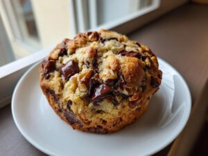 A thick, gooey levain bakery chocolate chip cookie loaded with large chocolate chunks and walnuts, served on a white plate.