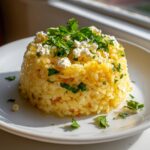 A perfectly molded serving of yellow Mediterranean rice topped with crumbled feta cheese and fresh parsley.