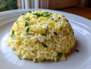 A dome-shaped serving of bright yellow mediterranean rice mixed with white cheese crumbles and fresh parsley.