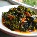 A close-up of rich, slow-cooked collard greens served in a white bowl with savory shredded meat and broth.