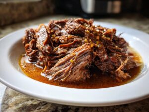 Close-up of shredded, tender Mississippi pot roast served in its rich, savory juices on a white plate.