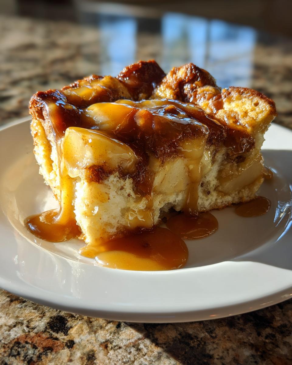 A close-up of a moist slice of apple bread pudding generously topped with dripping caramel sauce.