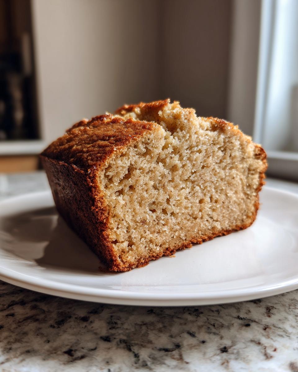 A thick slice of moist banana bread recipe showing a tender crumb and golden brown crust, served on a white plate.