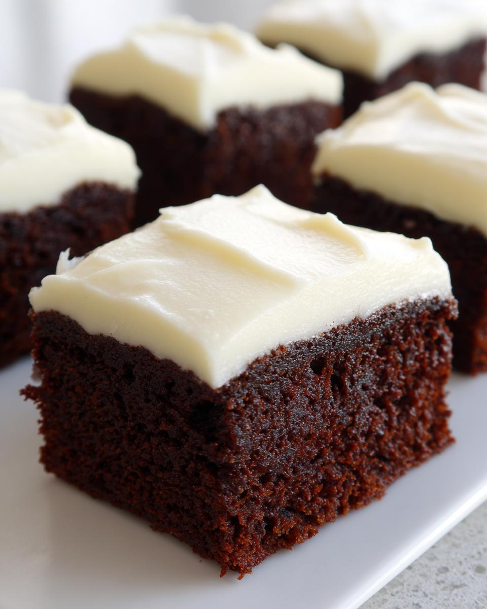 Close-up of a square piece of dark, moist gingerbread brownies topped with thick white cream cheese frosting.