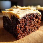 Close-up of a moist, dark slice of gingerbread cake topped with thick, creamy frosting.