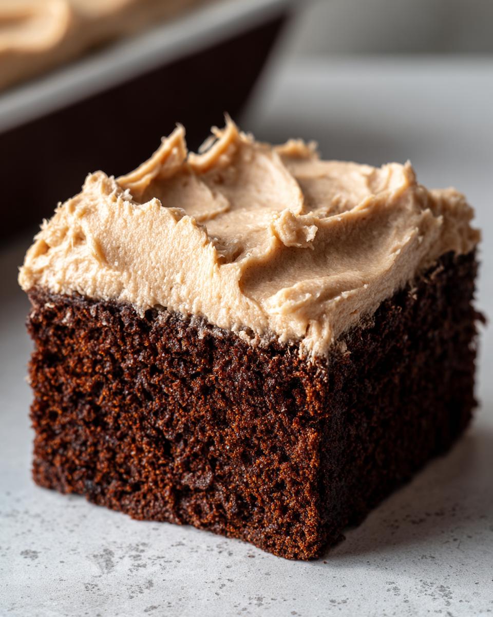 Close-up of a square slice of dark, moist gingerbread cake topped with thick, light brown frosting.