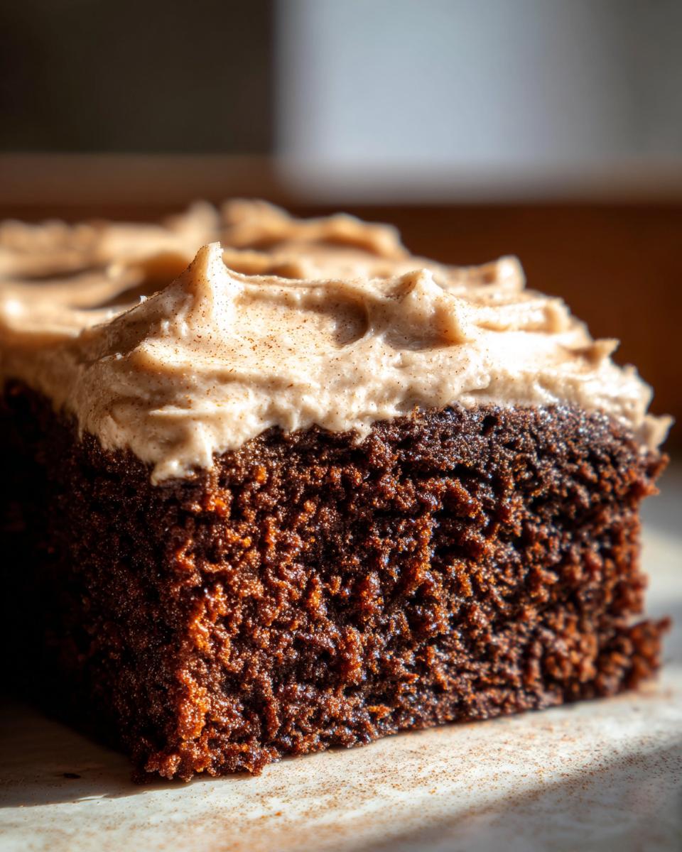 Close-up of a rich, dark slice of moist gingerbread cake topped with thick, spiced cream cheese frosting.
