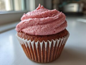 Close-up of a moist strawberry cupcake with a generous swirl of pink strawberry frosting in a white paper liner.