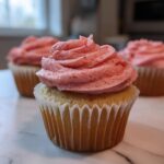 Close-up of a moist strawberry cupcake topped with a generous swirl of pink strawberry frosting.