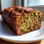 A close-up view of a freshly baked loaf of moist zucchini banana bread showing the tender crumb and green zucchini pieces.