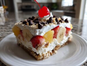 A delicious slice of no-bake banana split cake topped with whipped cream, fruit, chocolate chips, and a maraschino cherry.