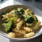 Close-up of creamy broccoli pasta made with fusilli, topped with grated cheese and pepper.