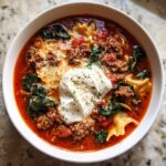 Close-up of a hearty bowl of one pot lasagna soup topped with a dollop of ricotta cheese and ground meat.