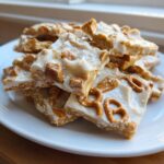 A stack of homemade peanut butter pretzel bark squares topped with white chocolate and sea salt.