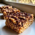 Close-up of a thick peanut butter rice krispie treats square topped with melted chocolate drizzle.