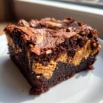 A close-up of a fudgy peanut butter swirl brownies square on a white plate, showing the cracked top and creamy peanut butter pockets.