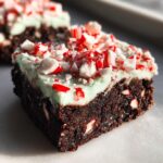 A decadent square of peppermint brownies topped with light green mint frosting and crushed candy canes.