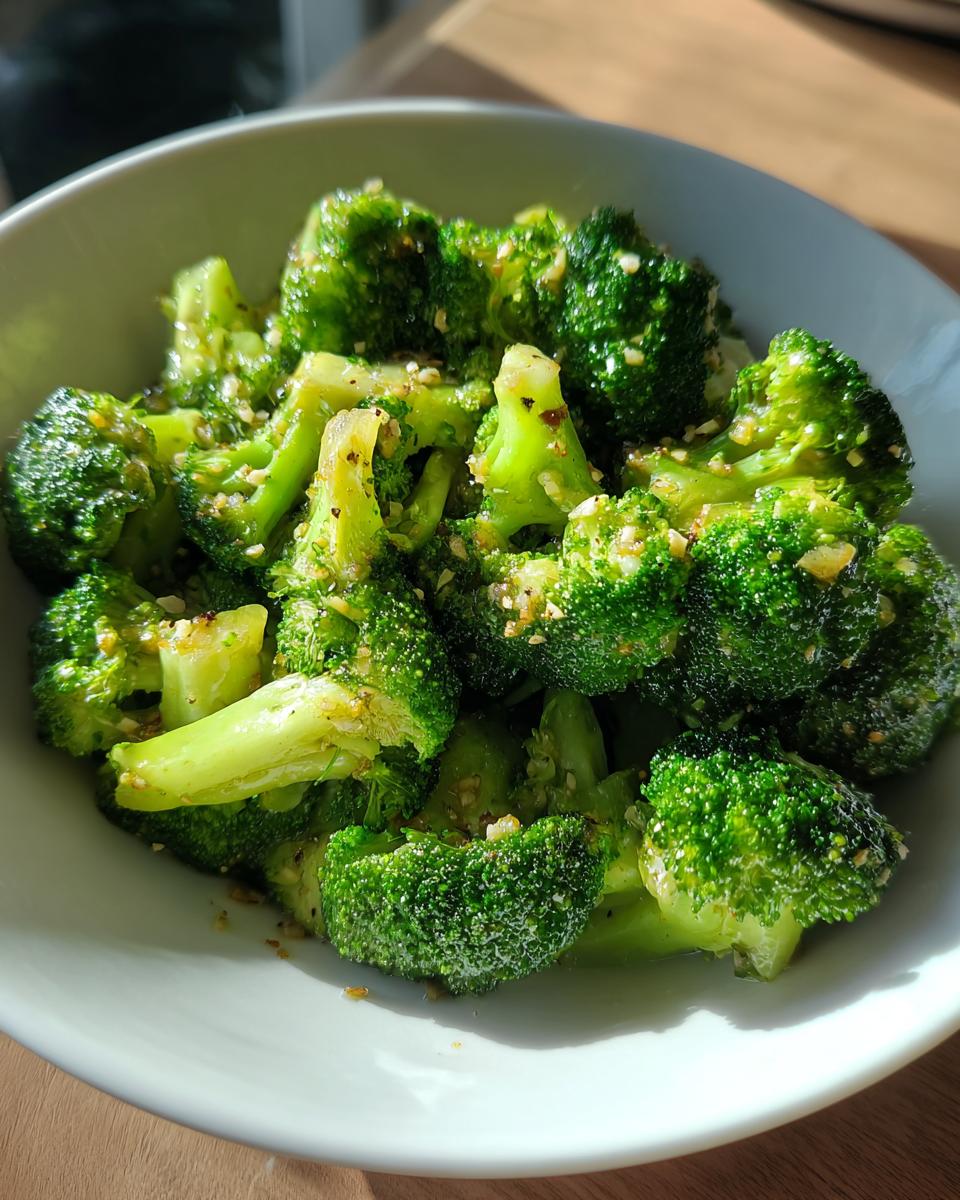 Close-up of vibrant green steamed broccoli florets seasoned with spices in a white bowl.