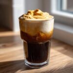 A tall glass filled with dark cold brew coffee topped with thick, airy pumpkin cream cold brew foam.