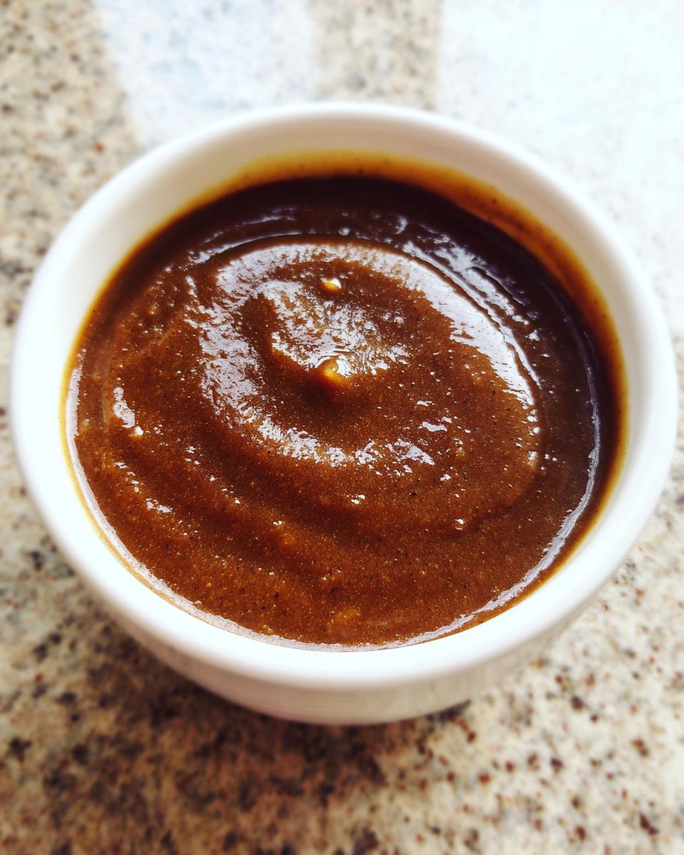 Close-up of thick, rich homemade brown gravy served in a small white bowl on a speckled countertop.
