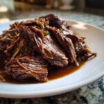 Close-up of tender, shredded mississippi pot roast served on a white plate with rich brown gravy.
