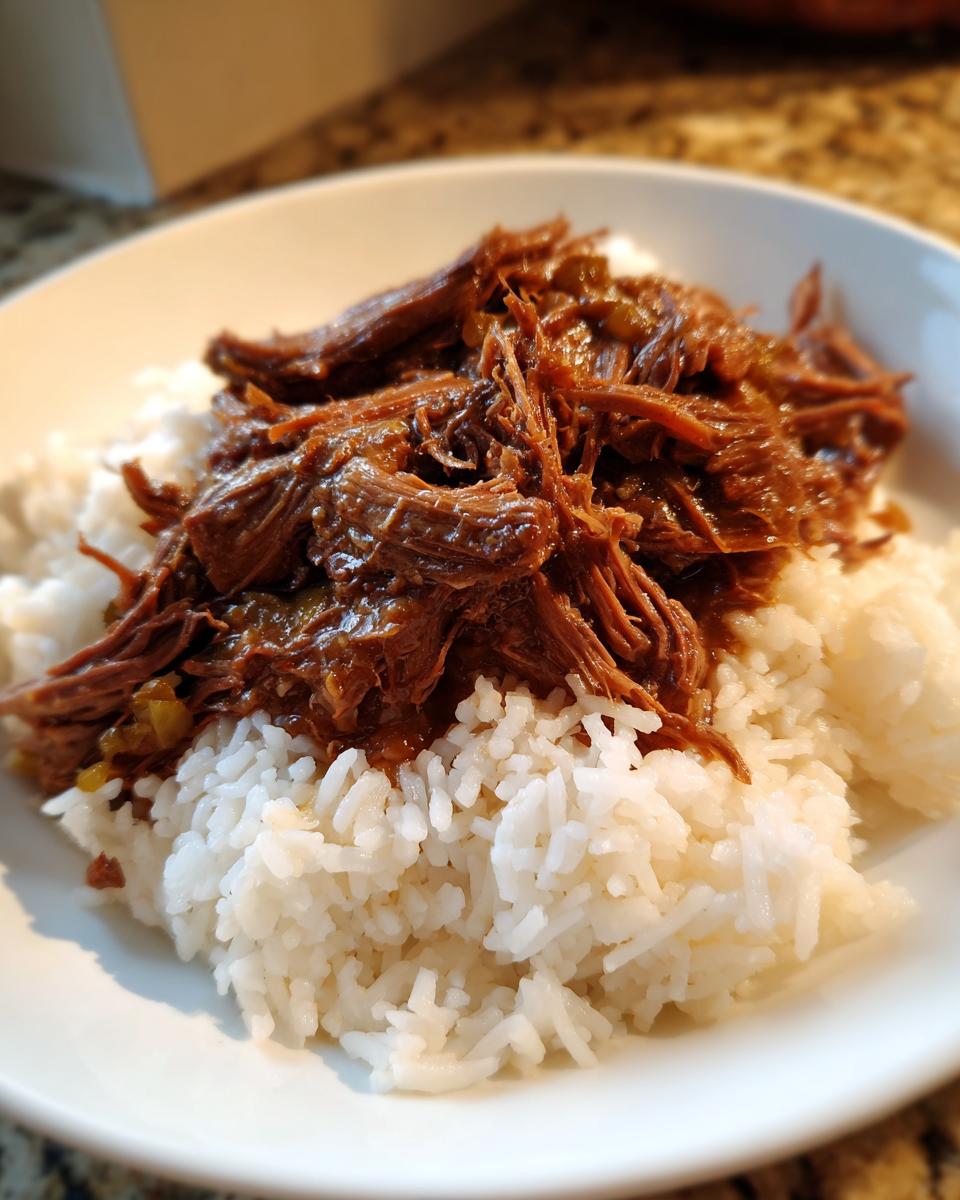 A close-up of tender, shredded mississippi pot roast served generously over a bed of fluffy white rice in a white bowl.