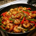 Close-up of seasoned shrimp fajitas cooking with colorful bell peppers and onions in a black skillet.