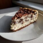 A perfect slice of chocolate chip cheesecake with a graham cracker crust, topped with chocolate chips.