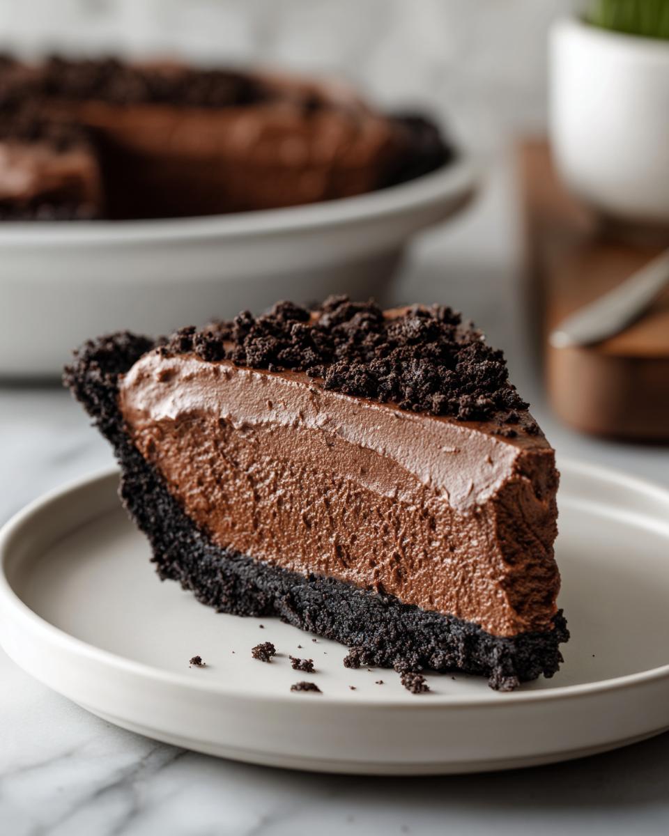 A close-up of a perfect slice of chocolate mousse pie with a dark cookie crust and crumb topping.