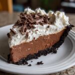 A decadent slice of chocolate mud pie featuring a dark crust, thick chocolate filling, whipped cream, and chocolate shavings.