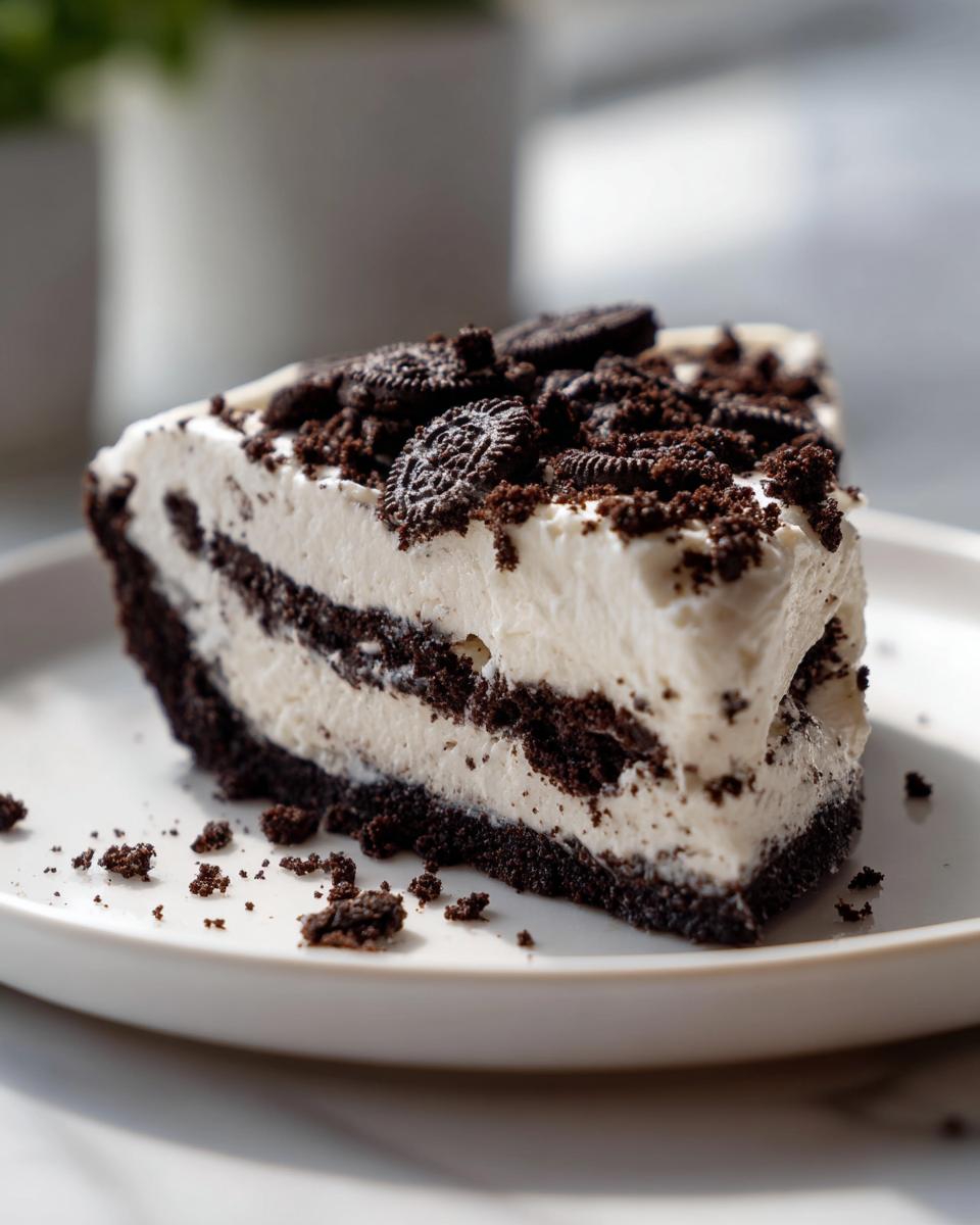 A decadent slice of no-bake Oreo pie featuring layers of cream filling and chocolate crust, topped with crushed Oreos.