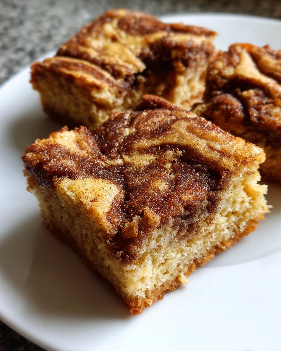 A close-up shot of a square piece of snickerdoodle blondies with a rich cinnamon swirl topping on a white plate.