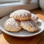 A stack of soft ricotta cookies drizzled with white glaze and sprinkled with coarse sugar on a light plate.
