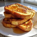 A stack of thick, golden-brown sourdough french toast slices drizzled generously with syrup.
