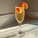 A fizzy, golden bellini recipe cocktail in a champagne flute, garnished with fresh peach slices.