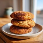 Three soft snickerdoodles stacked on a speckled ceramic plate, coated heavily in cinnamon sugar.